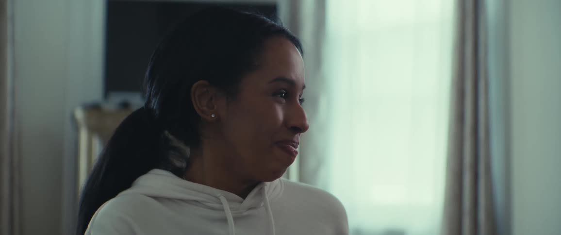 A young woman with dark hair in a ponytail and a white hoodie slightly smiling and then laughing
