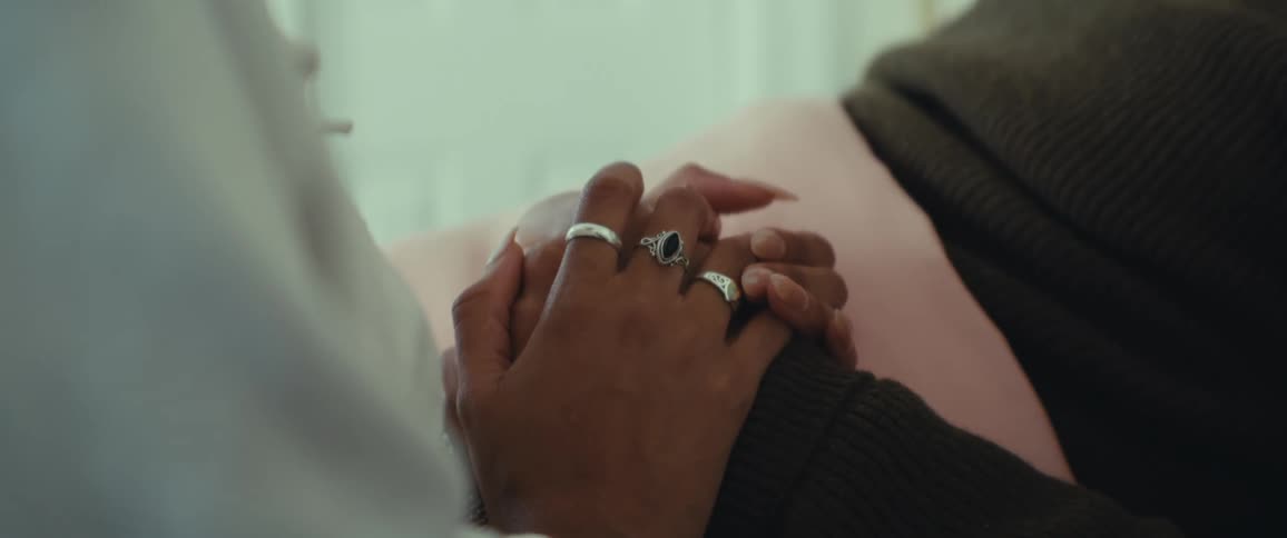 Woman sits and holds hands with a man lying on a bed during the day