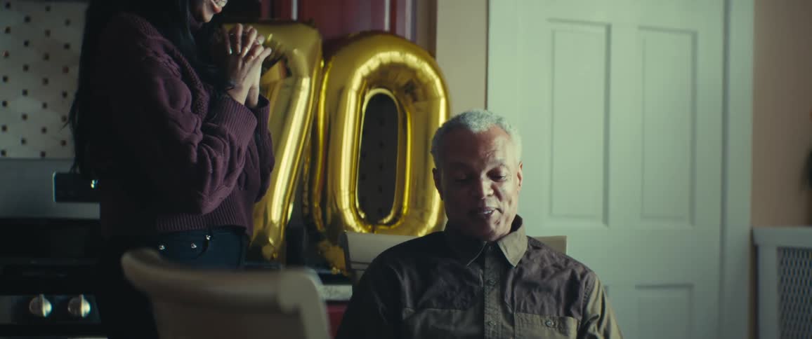 Adult daughter hugging elderly father who is sitting at a table with a birthday cake
