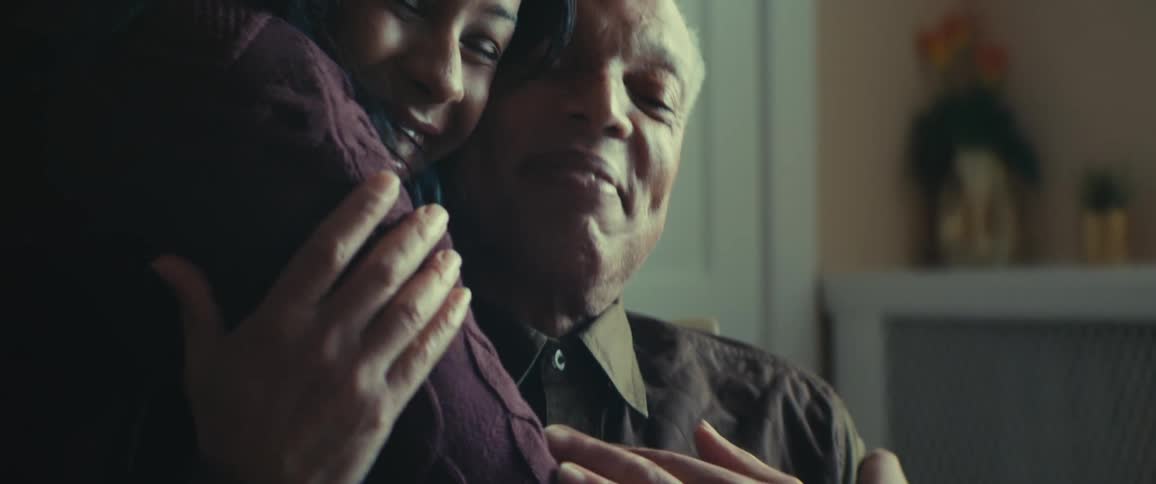 Elderly man blowing out the lit candles on a birthday cake and receiving a hug from a woman