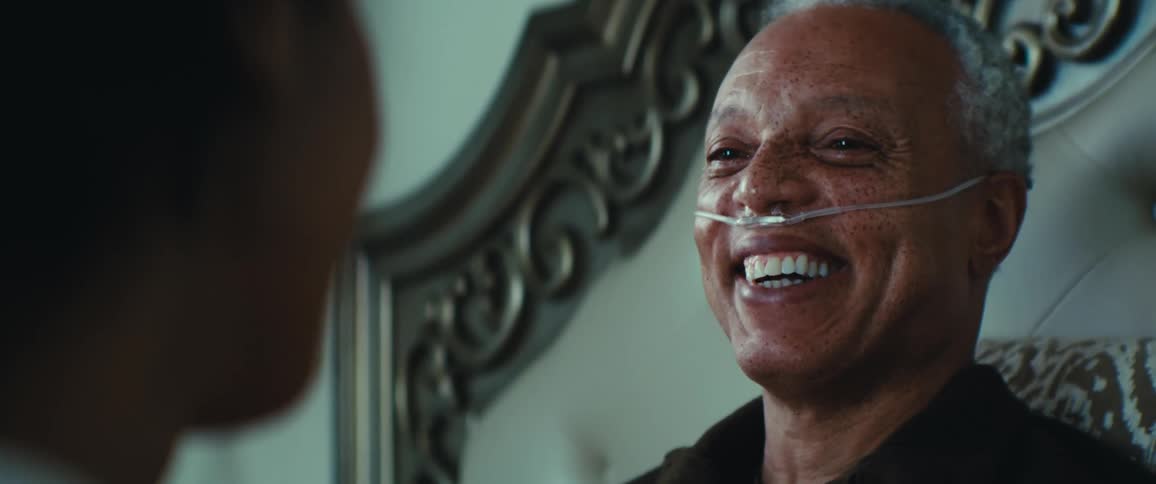 Elderly male invalid laughs while talking to a visitor in his bedroom