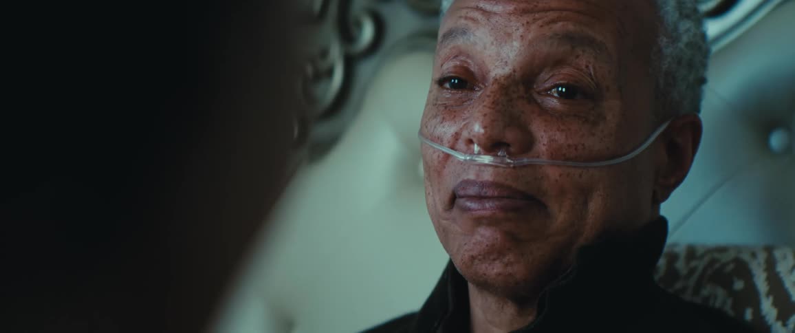 Elderly man with freckled skin smiles slightly while using a nasal oxygen catheter