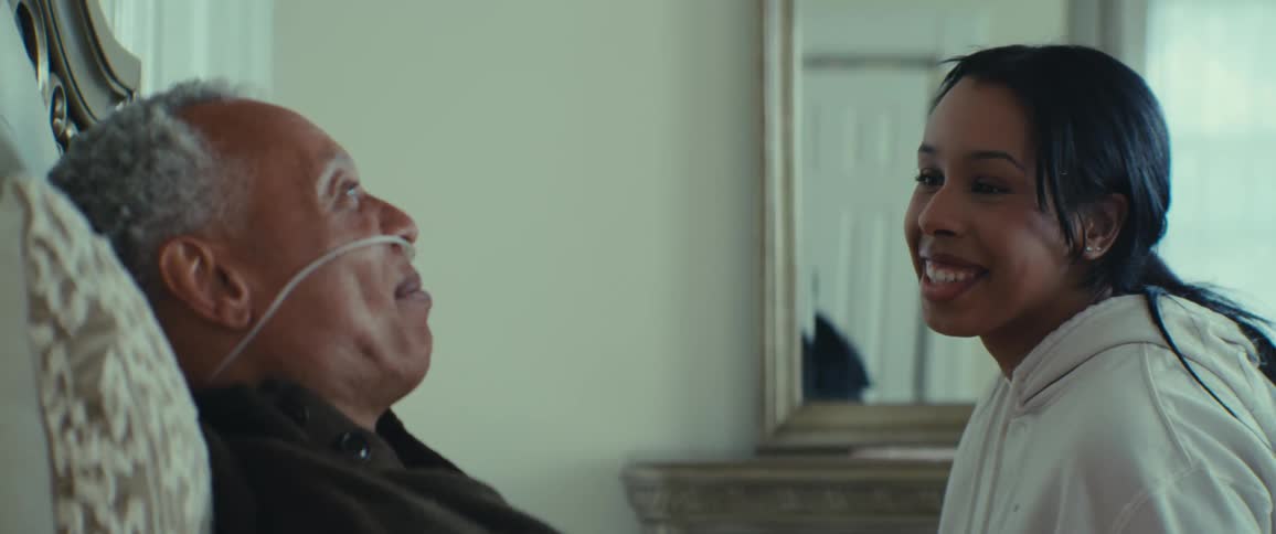 Smiling woman sitting talking to an elderly man who is lying in bed with a nasal oxygen catheter
