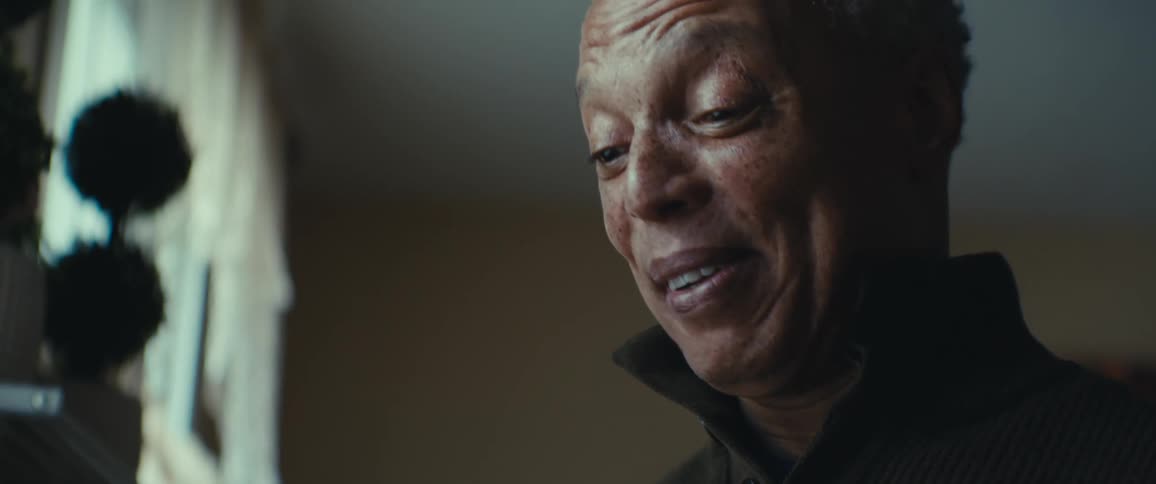 An older man with gray hair and freckles smiling softly and looking down