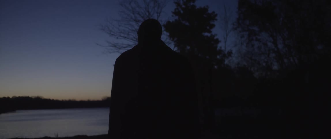 A silhouetted man walking towards a lake at dusk
