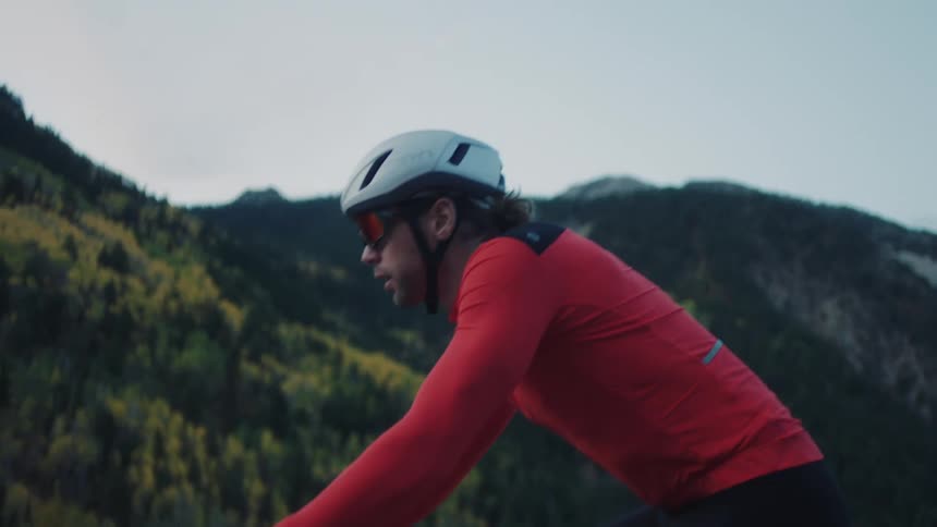 A person wearing a white helmet and a red longsleeve cycling jersey is riding a bicycle in a mountainous
