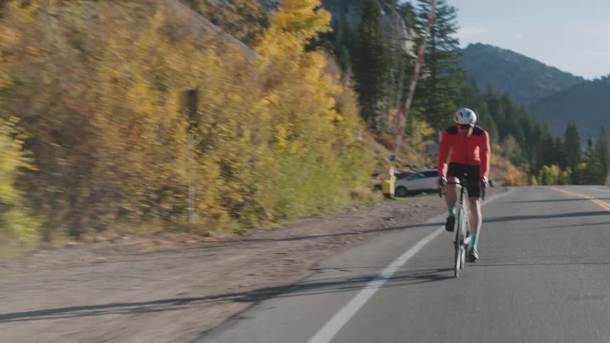 A man rides his bike up a mountain road as the leaves change colors