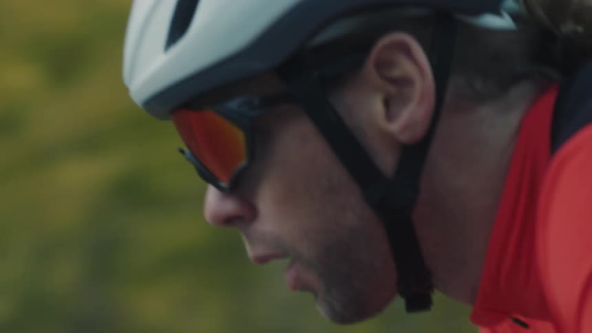 Male cyclist pedals along a highway passing the woods in autumn