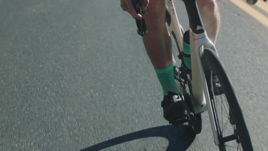 A cyclist wearing a white helmet and an orange jacket is riding on a road in the countryside