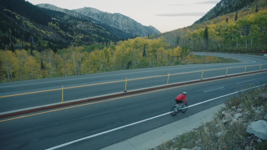 A car disappears as it comes around a bend then a cyclist heads down the mountain in the other direction