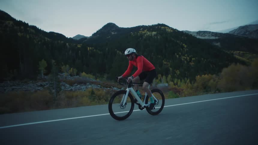 Man cycling on asphalt in an environment surrounded by mountains on a cloudy day