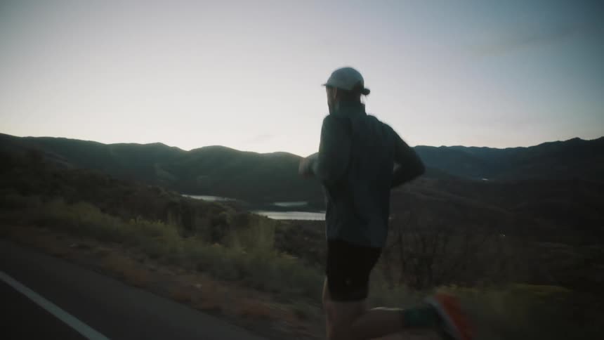 Man runs along a highway overlooking a valley after dusk