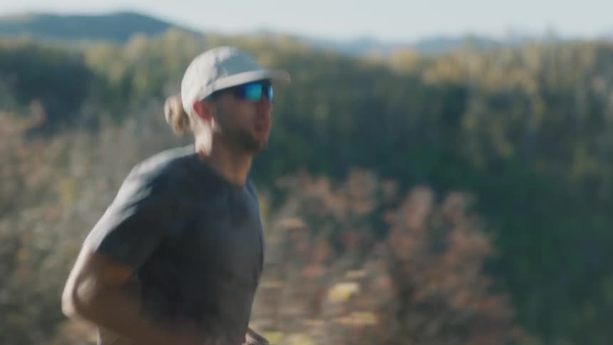 Runner wearing a cap and sunglasses walks determinedly along an outdoor trail