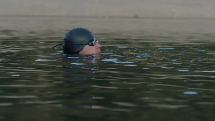 Man with swimming cap and goggles floating in a calm lake