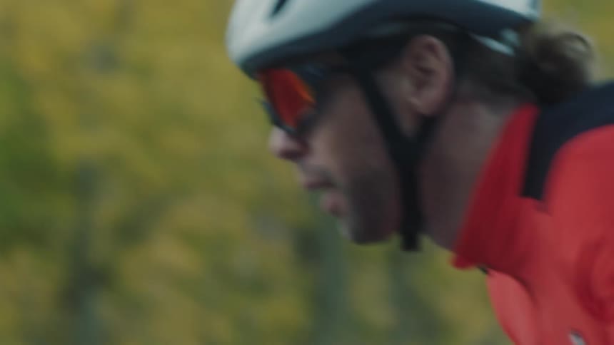 Male cyclist pedals a bicycle along a highway past the woods during the fall