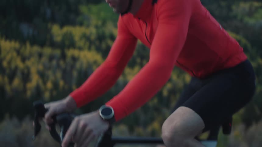 A cyclist wearing a red jacket is shown riding a bike against a mountain backdrop