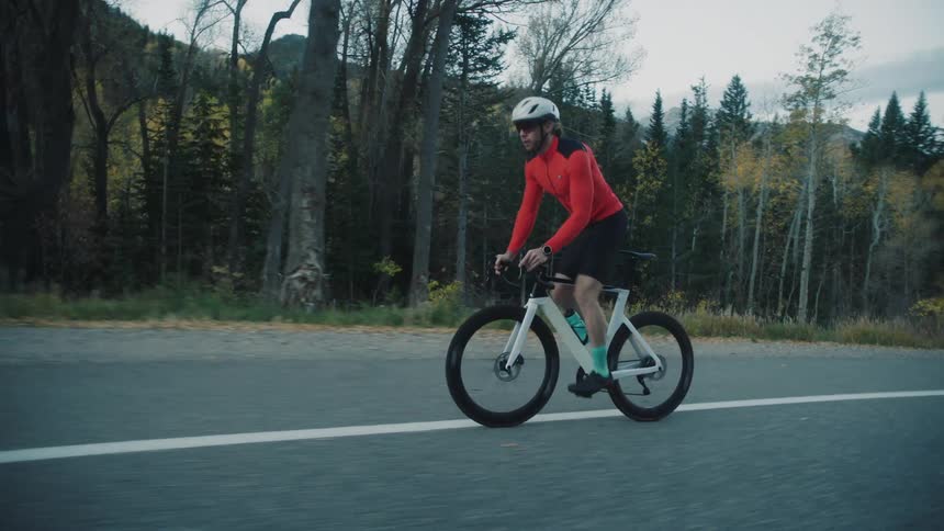 Cyclist riding on a paved road surrounded by mountains and forests