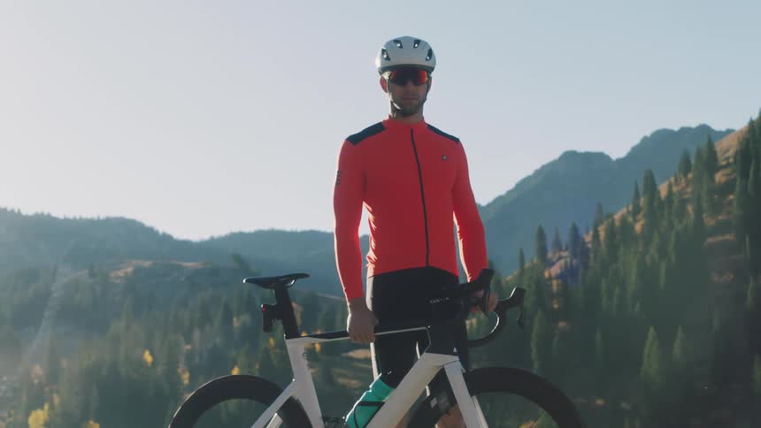Male cyclist stands next to his bicycle near forested mountains on a foggy day