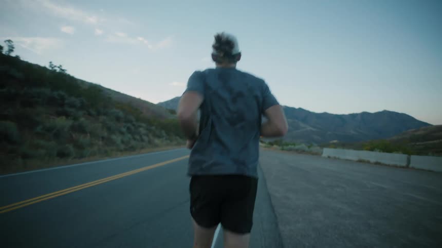 Man starting to run on a highway surrounded by mountains
