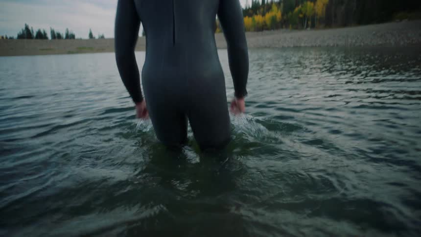 Wetsuit diver walks in calm waters under a partly cloudy sky