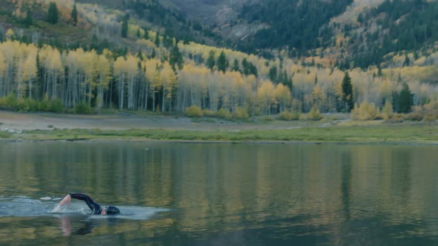 A person swims in a lake surrounded by trees and mountains