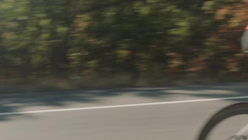 A cyclist wearing a red outfit and a white helmet is riding a bicycle on a winding road surrounded by trees and mountains