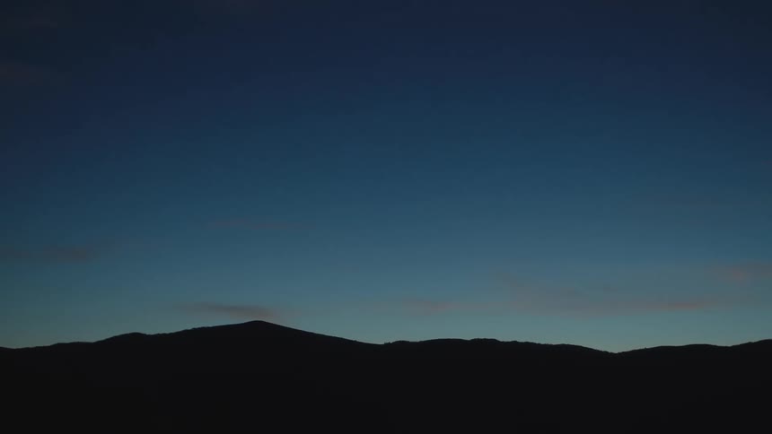 A silhouette of a mountain range is visible against a deep blue gradient sky at dusk