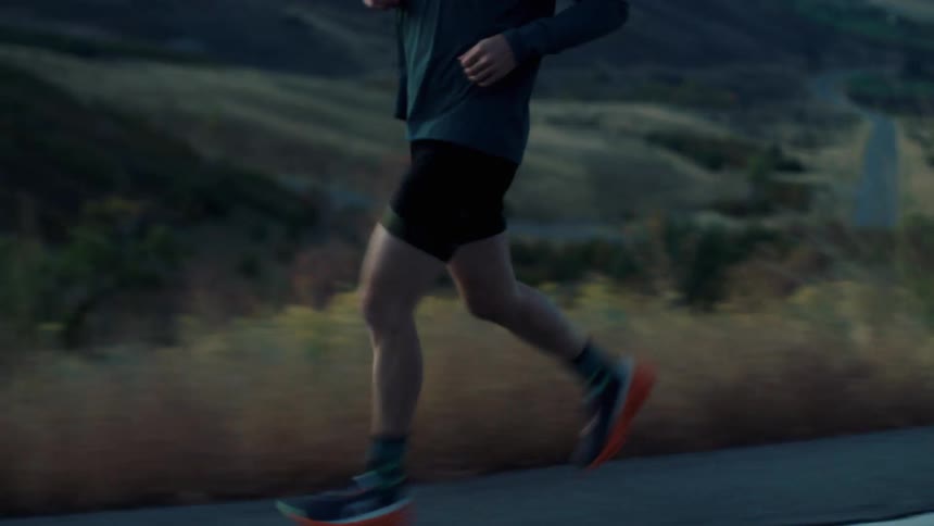 Runner continues steadily at dusk with the dark mountains in the background contrasting with his moving silhouette
