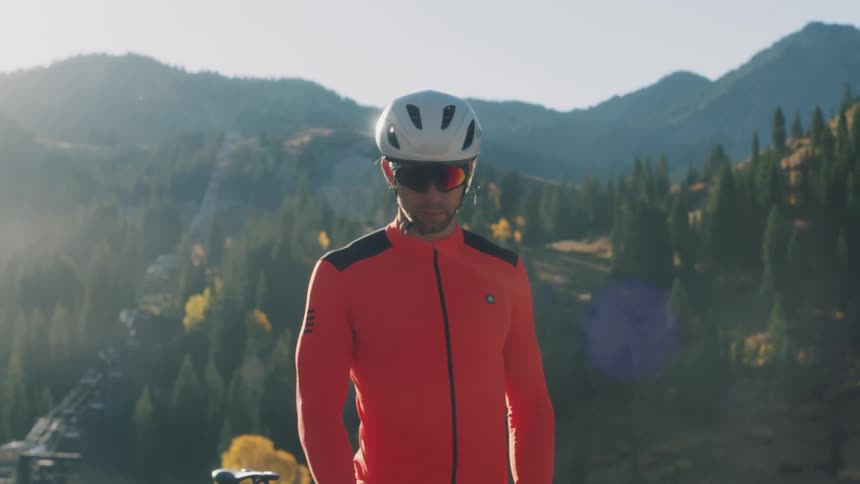 A man is standing with mountains and forest behind him