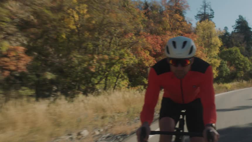 A man is cycling along a remote mountain highway on a sunny autumn day