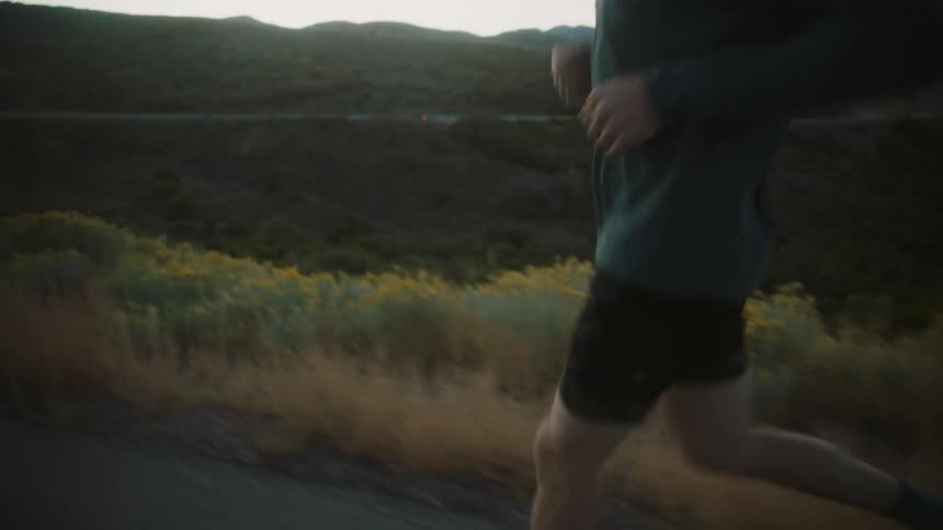 Man in glasses and cap running with mountain landscape in a morning