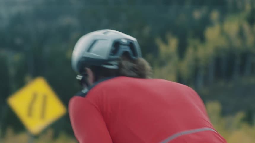 Cyclist in a red shirt and helmet riding on a road surrounded by mountains and vegetation