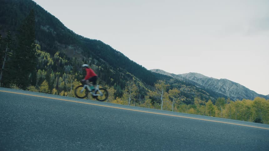 Lone cyclist pedals along a deserted road surrounded by towering mountains and autumngolden trees