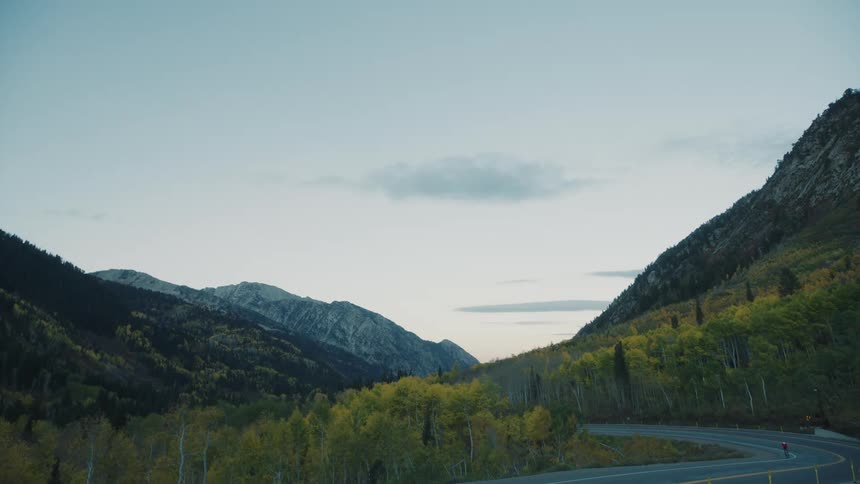Scene of a highway with a vehicle passing by and a cyclist in an environment surrounded by green mountains