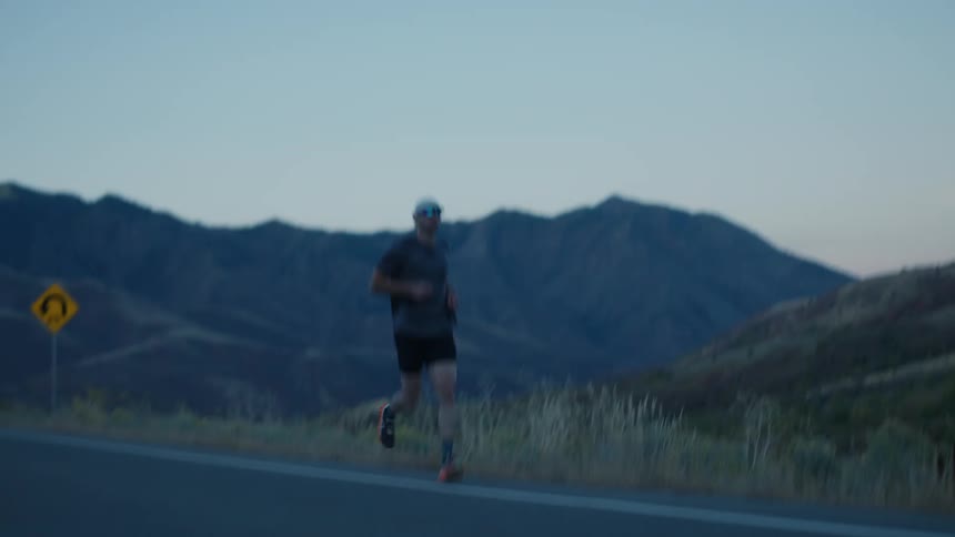 A man is running on the side of the road by the mountains