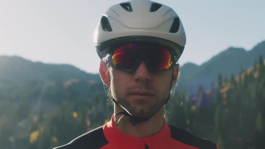 Man in a bicycle helmet slowly raises his head with the mountains behind him