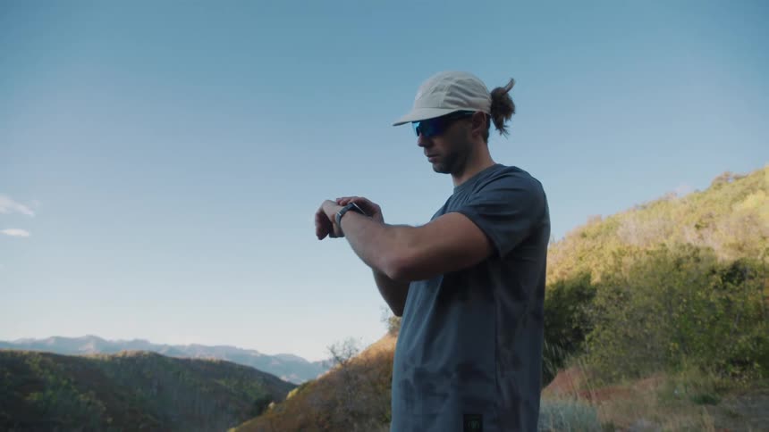 Man in cap on a mountain trail adjusting his wristwatch