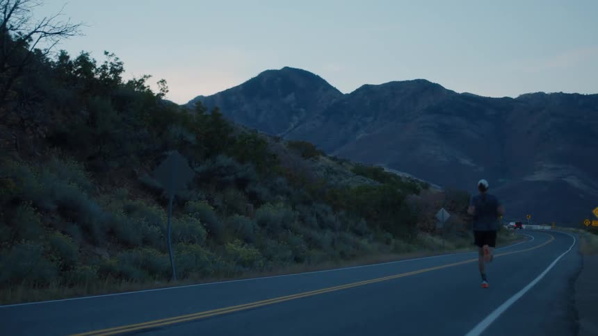 Man in cap running on asphalt highway in mountainous environment