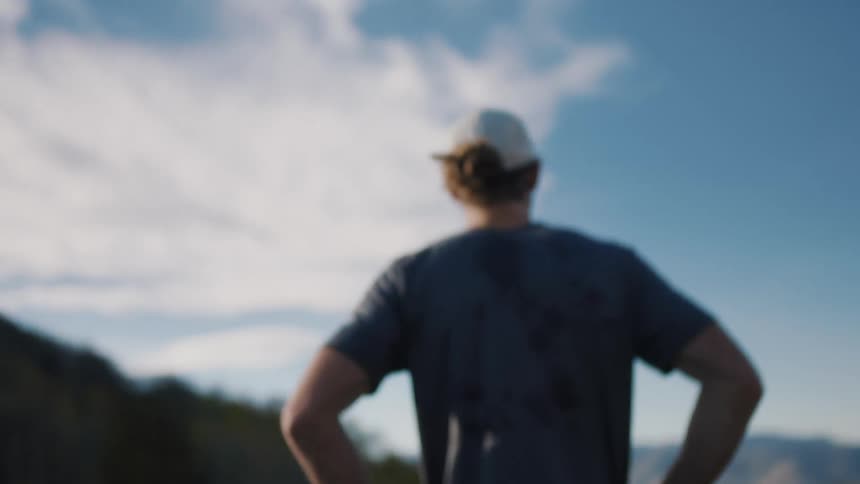 Man moves his hands from his hips to his head as he rests looking at the mountains