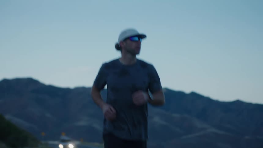 A man is jogging on a road with traffic in the mountains