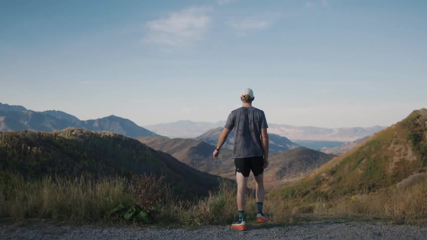Man running and stopping putting his hands on his hips while enjoying a view of a mountain valley