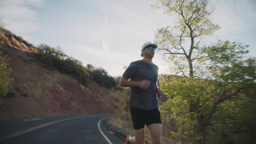 A man is jogging up a remote highway on a sunny autumn day