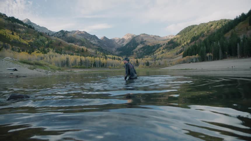 Man swimming in a calm lake surrounded by mountains