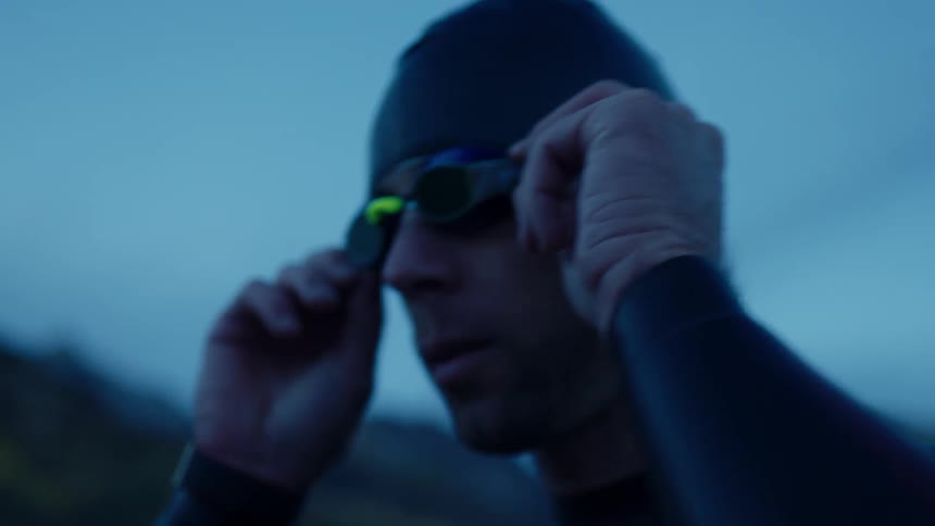 Portrait of a man putting on swimming goggles while standing outdoors on a dark morning