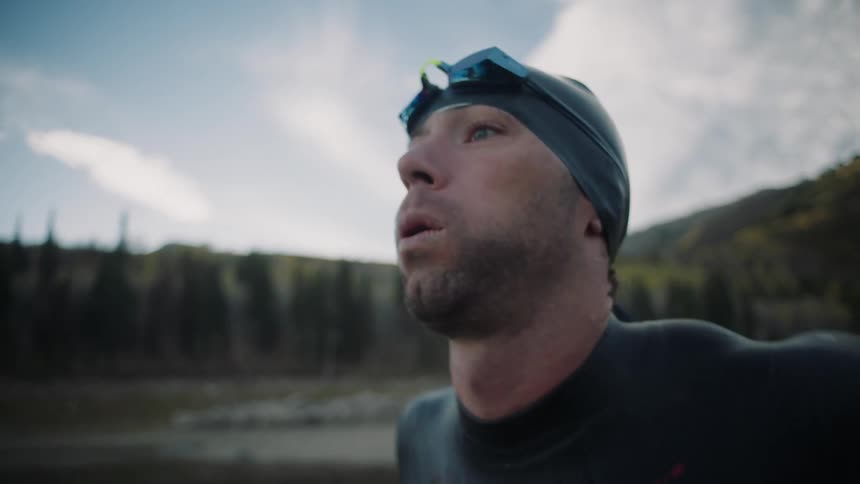 A man stretches and puts on his goggles as he gets ready to go into a lake