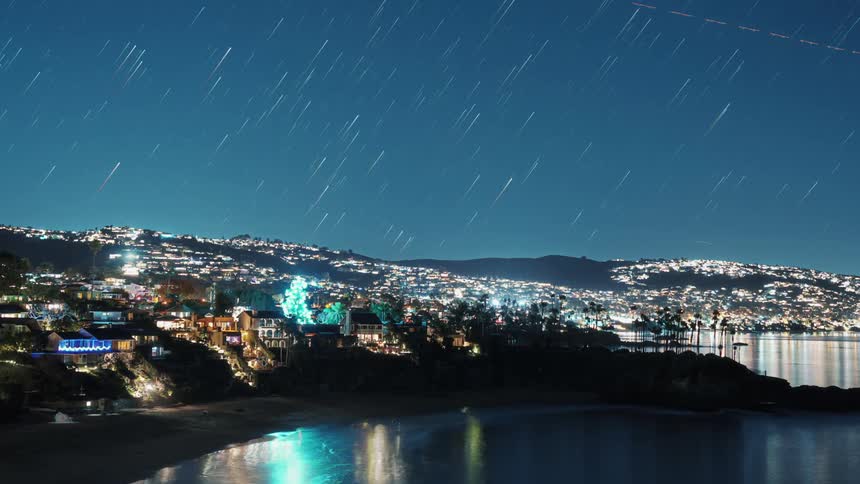 Night landscape of a beach with a starry sky and in the background an illuminated city between hills