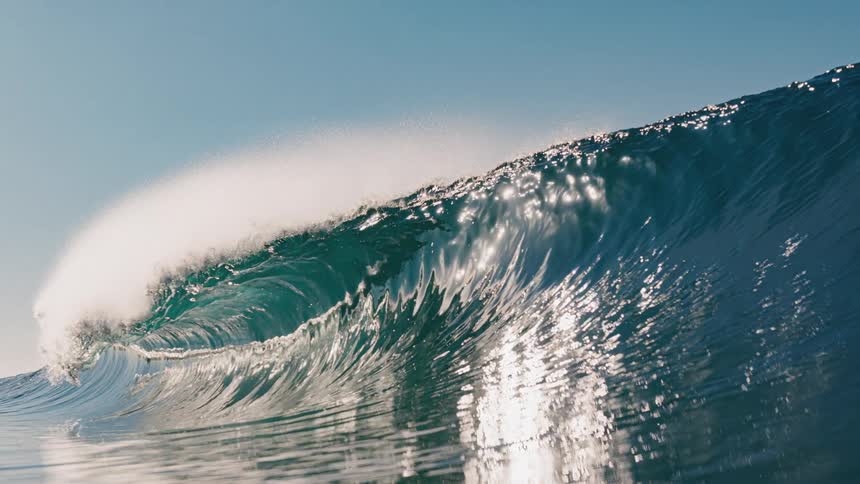 Majestic wave rises shining in the sun its crest sculpted by the wind and the foam dissolving into the air