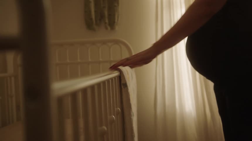 Expectant mother hangs a baby quilt on the side of a crib in the baby room
