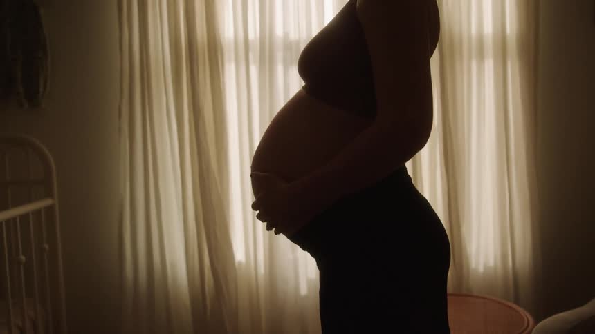 A pregnant woman massages her belly by the crib