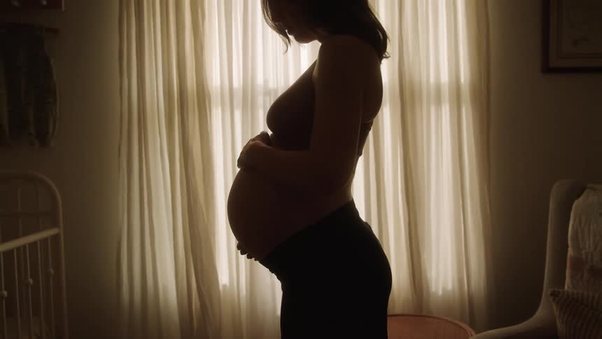 Silhouette of a pregnant woman running her hands over her belly while standing in the nursery